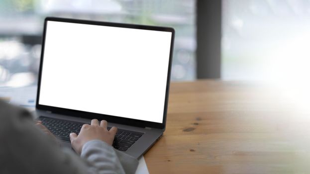 Mockup image of a woman using and typing on laptop with blank white desktop screen on wooden table.