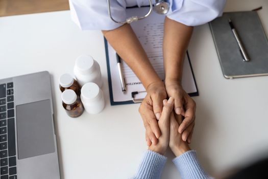 Doctor giving hope. Close up shot of young female physician leaning forward to smiling elderly lady patient holding her hand in palms. Woman caretaker in white coat supporting encouraging old person.