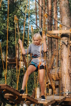 A girl passes an obstacle in a rope town. A girl in a forest rope park.