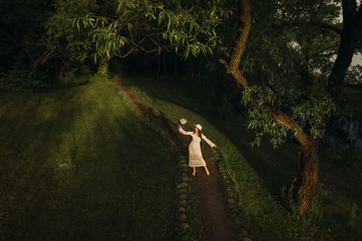 Portrait of a beautiful woman in a white dress and a hat with lilies of the valley. A girl in nature. Spring flowers.