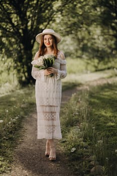 Portrait of a beautiful woman in a white dress and a hat with lilies of the valley. A girl in nature. Spring flowers.