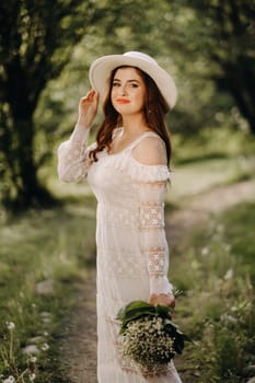 Portrait of a beautiful woman in a white dress and a hat with lilies of the valley. A girl in nature. Spring flowers.