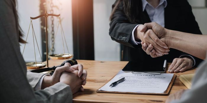 Close up of woman lawyer hand and man client shaking hand collaborate on working agreements with contract documents at the office..