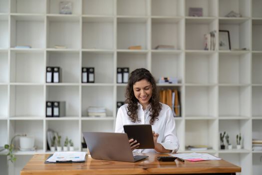 Pretty, charming woman using, browsing, typing, searching, expertising, working online on computer and tablet in workplace, using wi-fi internet.