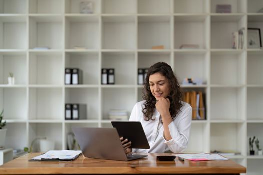 Pretty, charming woman using, browsing, typing, searching, expertising, working online on computer and tablet in workplace, using wi-fi internet.