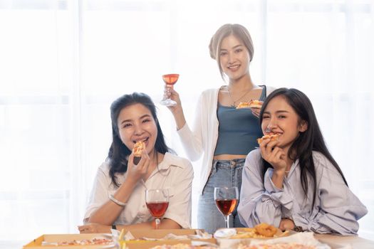 Group of Asian friends gather to celebrate Christmas with champagne and eating pizza at home. Joy of holiday party with friends or colleague concept.