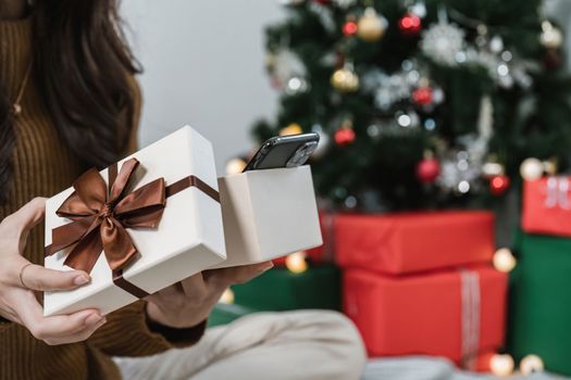 Close up woman opening present near Christmas tree. Happy holidays and New Year.