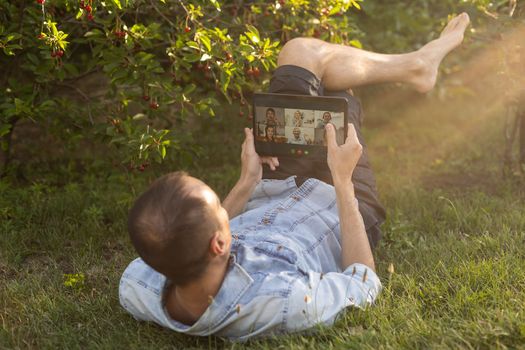 Young Man with a Tablet Computer on the Green Leaves Background outdoor