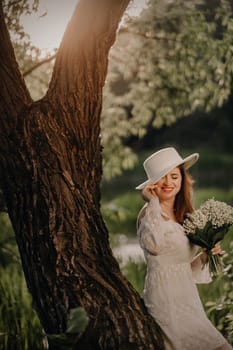 Portrait of a beautiful woman in a white dress and a hat with lilies of the valley. A girl in nature. Spring flowers.