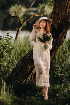 Portrait of a beautiful woman in a white dress and a hat with lilies of the valley. A girl in nature. Spring flowers.