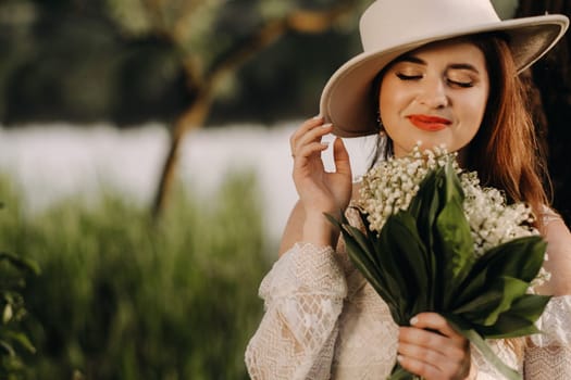 Portrait of a beautiful woman in a white dress and a hat with lilies of the valley. A girl in nature. Spring flowers.