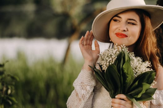 Portrait of a beautiful woman in a white dress and a hat with lilies of the valley. A girl in nature. Spring flowers.