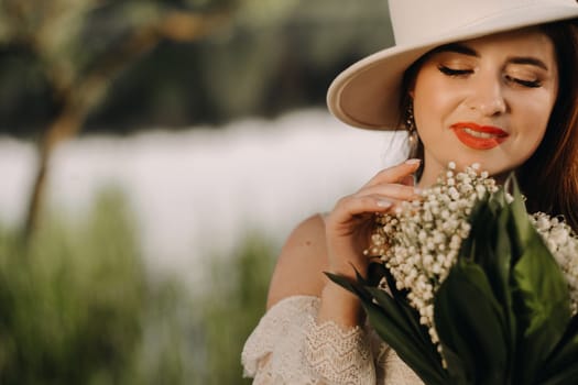 Portrait of a beautiful woman in a white dress and a hat with lilies of the valley. A girl in nature. Spring flowers.