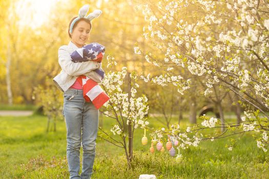 Girl kid in rabbit bunny ears on head with colored eggs and american flag. easter.