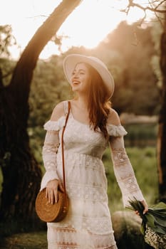 Portrait of a beautiful woman in a white dress and a hat with lilies of the valley at sunset. A girl in nature. Spring flowers.