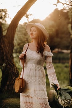 Portrait of a beautiful woman in a white dress and a hat with lilies of the valley at sunset. A girl in nature. Spring flowers.