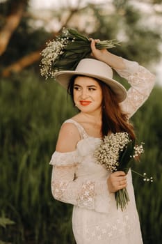 Portrait of a beautiful woman in a white dress and a hat with lilies of the valley. A girl in nature. Spring flowers.