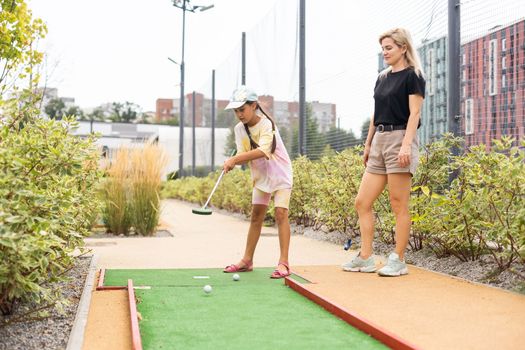 Mother playing with her cute daughter mini golf at outdoor playground