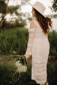 Portrait of a beautiful woman in a white dress and a hat with lilies of the valley. A girl in nature. Spring flowers.