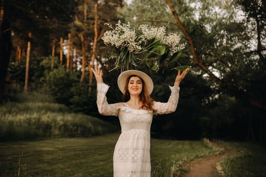 Portrait of a beautiful woman in a white dress and hat tossing lilies of the valley. A girl in nature. Spring flowers.