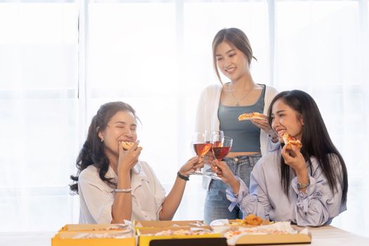 Group of Asian friends gather to celebrate Christmas with champagne and eating pizza at home. Joy of holiday party with friends or colleague concept.