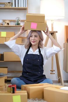 Startup small business entrepreneur SME or freelance Asian woman using a laptop with box, Young success Asian woman with her hand lift up, online marketing packaging box and delivery, SME concept..