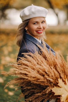 Portrait of a Girl in a jacket and birette with an autumn bouquet in an autumn park.