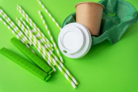 A green background on which a glass, tubes, a bag clip, a stand, a lid. Plastic and recycling concept, top view close-up. Place for an inscription