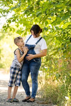 Pregnant woman walking countryside with her son. Child hugging his pregnant mother.