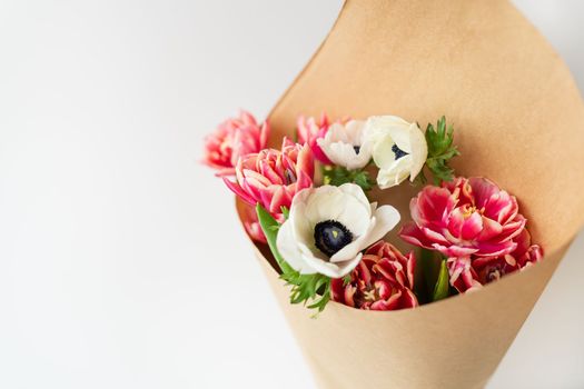 Beautiful red and white bouquet of tulips and anemones in kraft paper. The concept of spring and flowering. With copy space