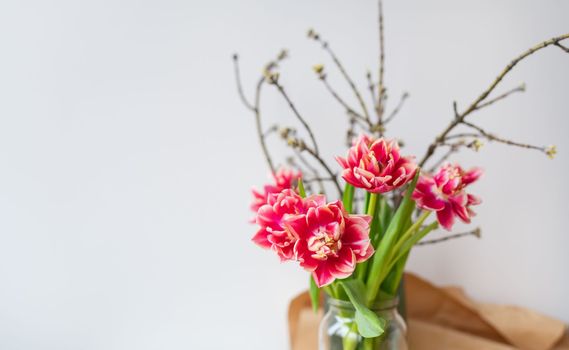 A beautiful spring bouquet of tulips stands in a vase along with spring branches. Surprise concept, birthday. Place for an inscription