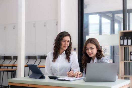 Two young Asian business woman talk, consult, discuss working with new startup project idea presentation analyze plan marketing and investment in the office..