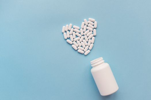 White pills in the shape of a heart and a white jar on a blue background. Pills for heart health. The concept of medicine and health care