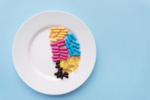 White plate with pills of nutritional supplements in different bright colors. Blue background, place for an inscription