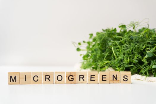 Vegetable pea sprouts, microgreens on white background, vegan health superfood. Inscription from wood letters microgreen