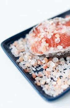 Fresh raw red salmon steak with large coarse pink salt prepared for baking on the grill lies on a blue plate. Healthy seafood food. Top view, place for an inscription