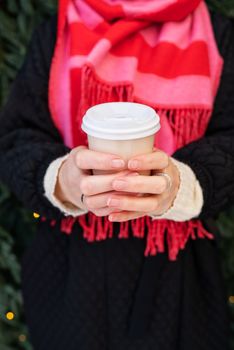 A young girl in a coat and a bright scarf holds hot coffee in her hands in a disposable cup. Coffee to go, hiking