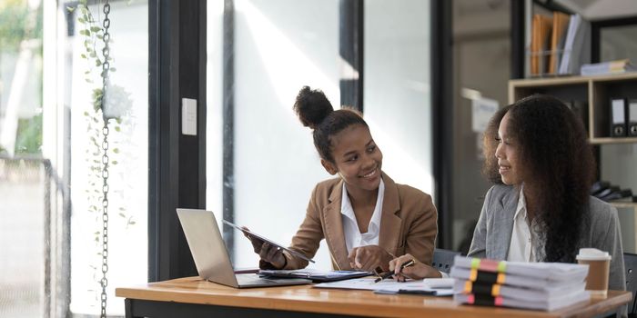 Two young Asian business woman talk, consult, discuss working with new startup project idea presentation analyze plan marketing and investment in the office..