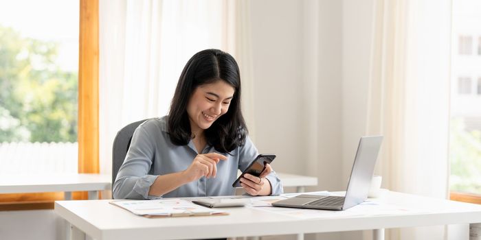 Business woman or accountant hand using mobile smart phone and laptop computer with documentary data graph paper on the table at modern home office. Online marketing concept