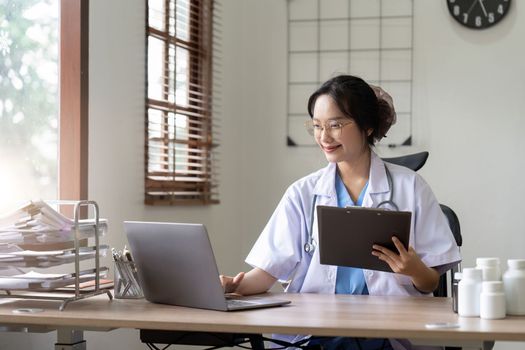 Asian doctor working with laptop in hospital and medical stethoscope, medicine on clipboard on workplace