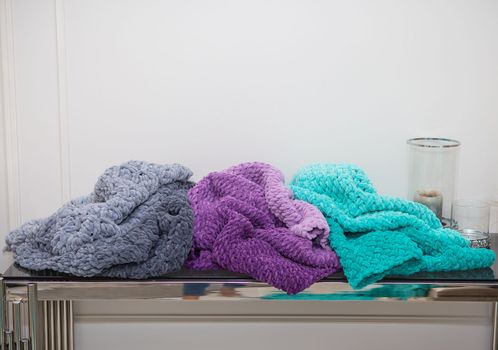 Beautiful plush multi-colored blankets of different colors lie together on the table along with a vase and candles. Close-up