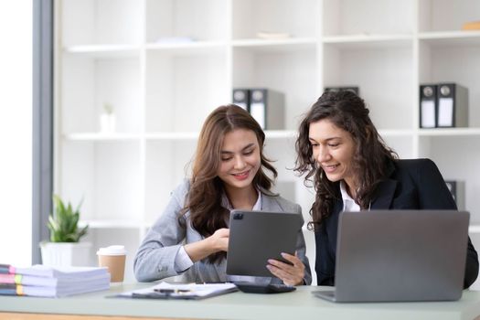 Two young Asian business woman talk, consult, discuss working with new startup project idea presentation analyze plan marketing and investment in the office..