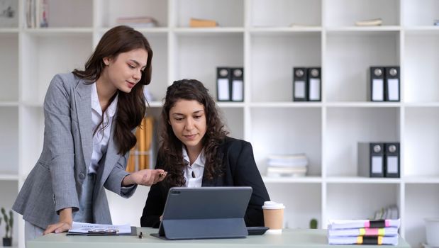 Two young Asian business woman talk, consult, discuss working with new startup project idea presentation analyze plan marketing and investment in the office..