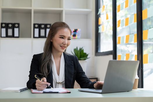 Charming asian businesswoman sitting working on laptop in office