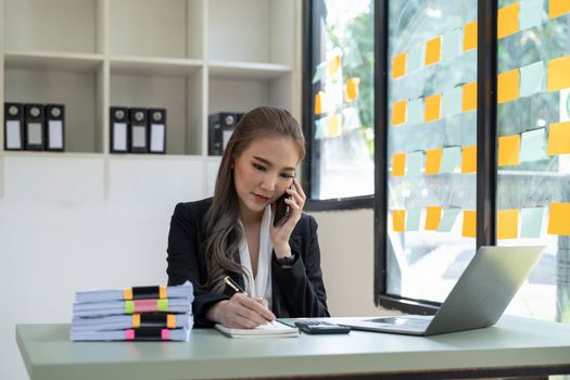 Portrait business accountant asian woman calling on phone and taking notes.