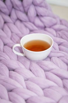 The concept of coziness and comfort is a pink-lavender knitted blanket with a white cup of hot tea on it. Place for inscription, vertical photo