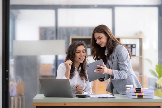 Two young Asian business woman talk, consult, discuss working with new startup project idea presentation analyze plan marketing and investment in the office..