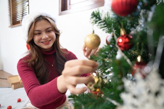 Happy young woman decorating the Christmas tree with ornaments.