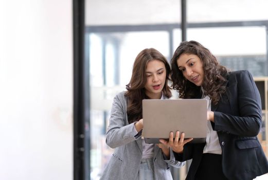 Two beautiful Asian businesswomen standing using digital tablet consulting and analyzing information in office work..