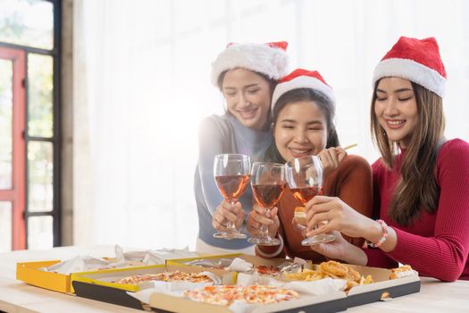 Group of Asian friends gather to celebrate Christmas with champagne and eating pizza at home. Joy of holiday party with friends or colleague concept.